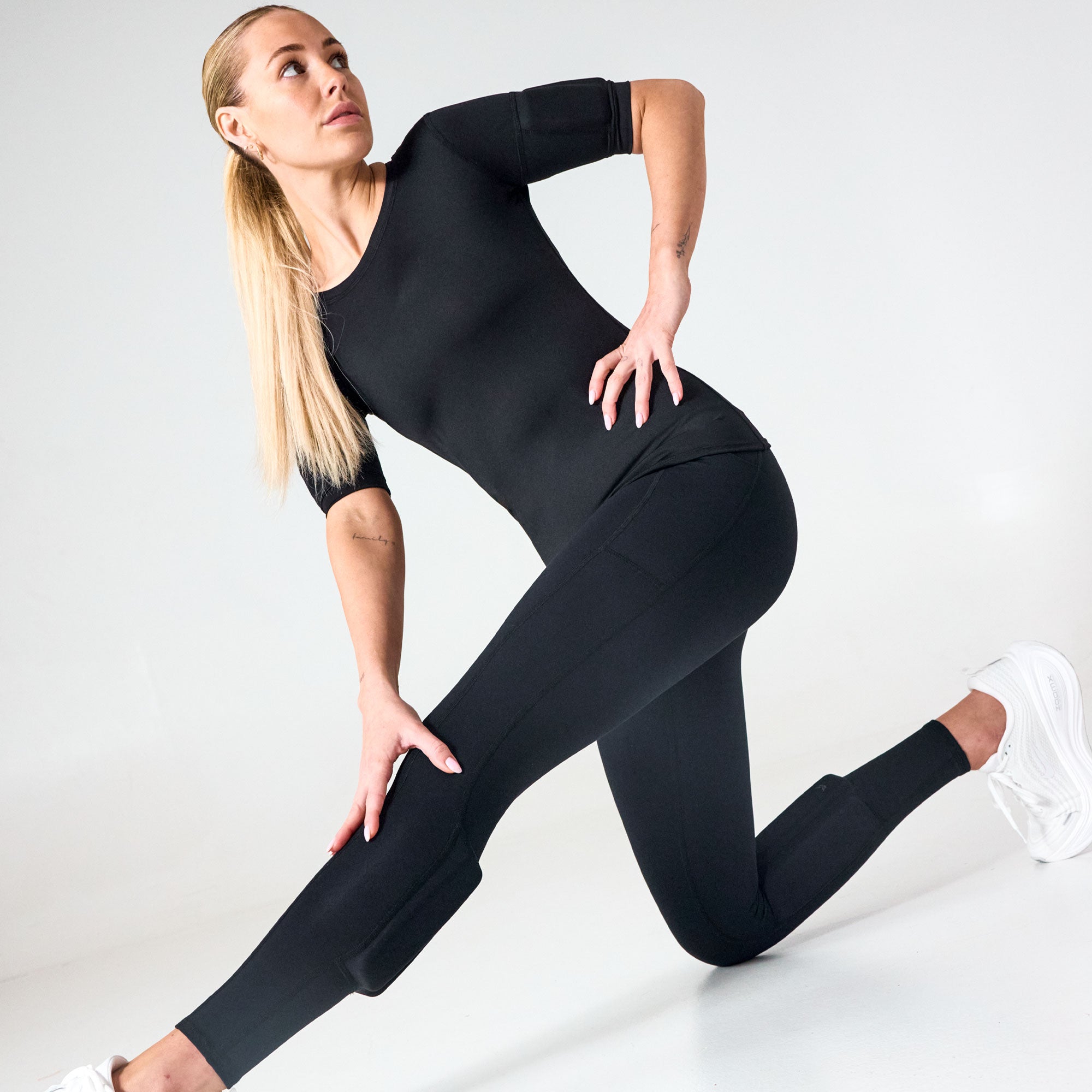 Woman stretching in a studio while wearing black PTP Pace Microweighted Leggings.