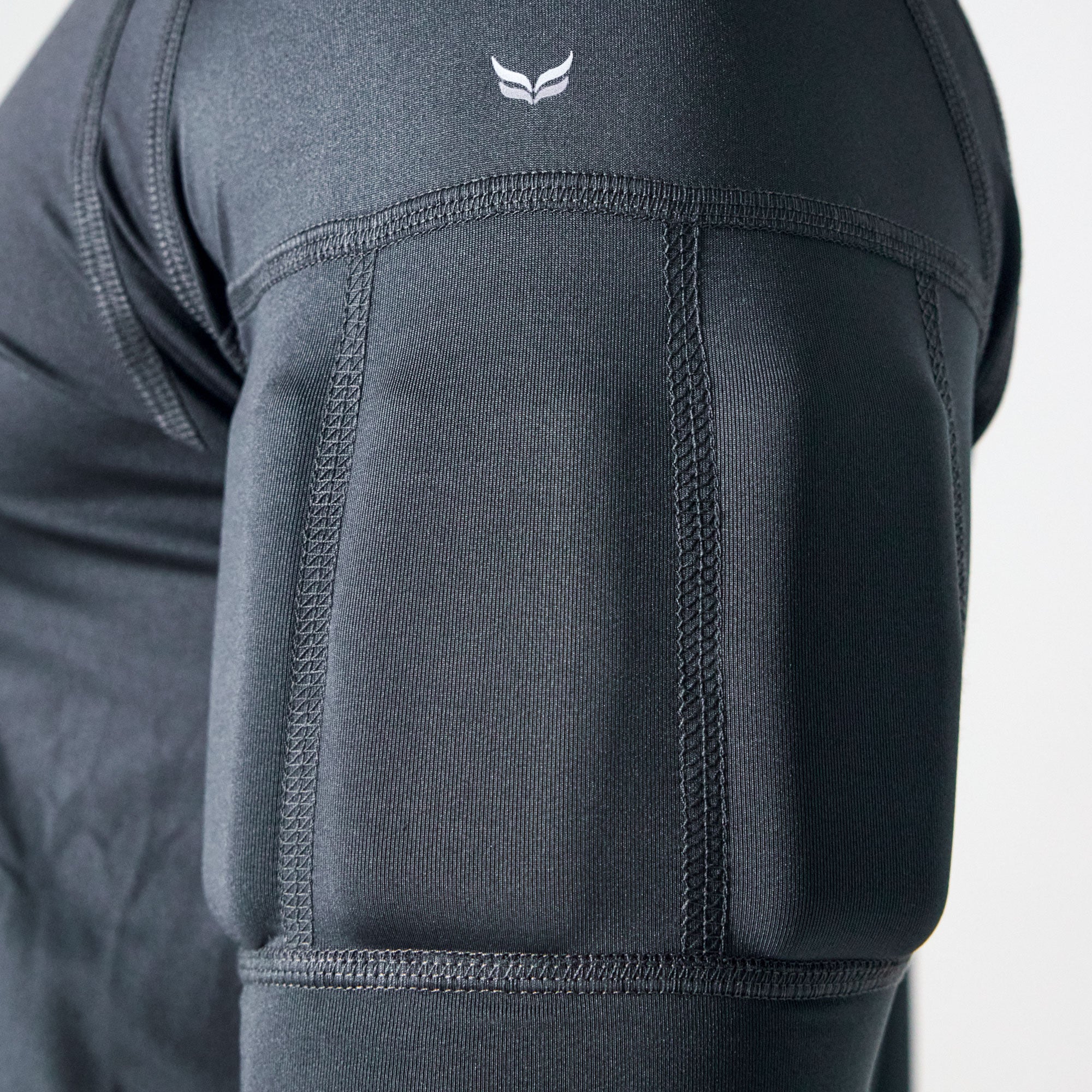 Close-up of a dark gray athletic compression sleeve on a person's upper arm, showing textured padding panels and a small white wing logo near the shoulder.