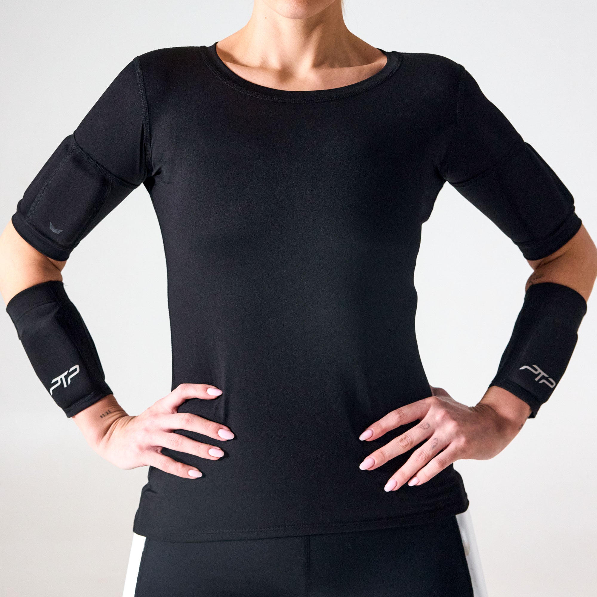 Woman wearing black PTP Motion Microweighted Arm Bands on both forearms, with hands on hips.