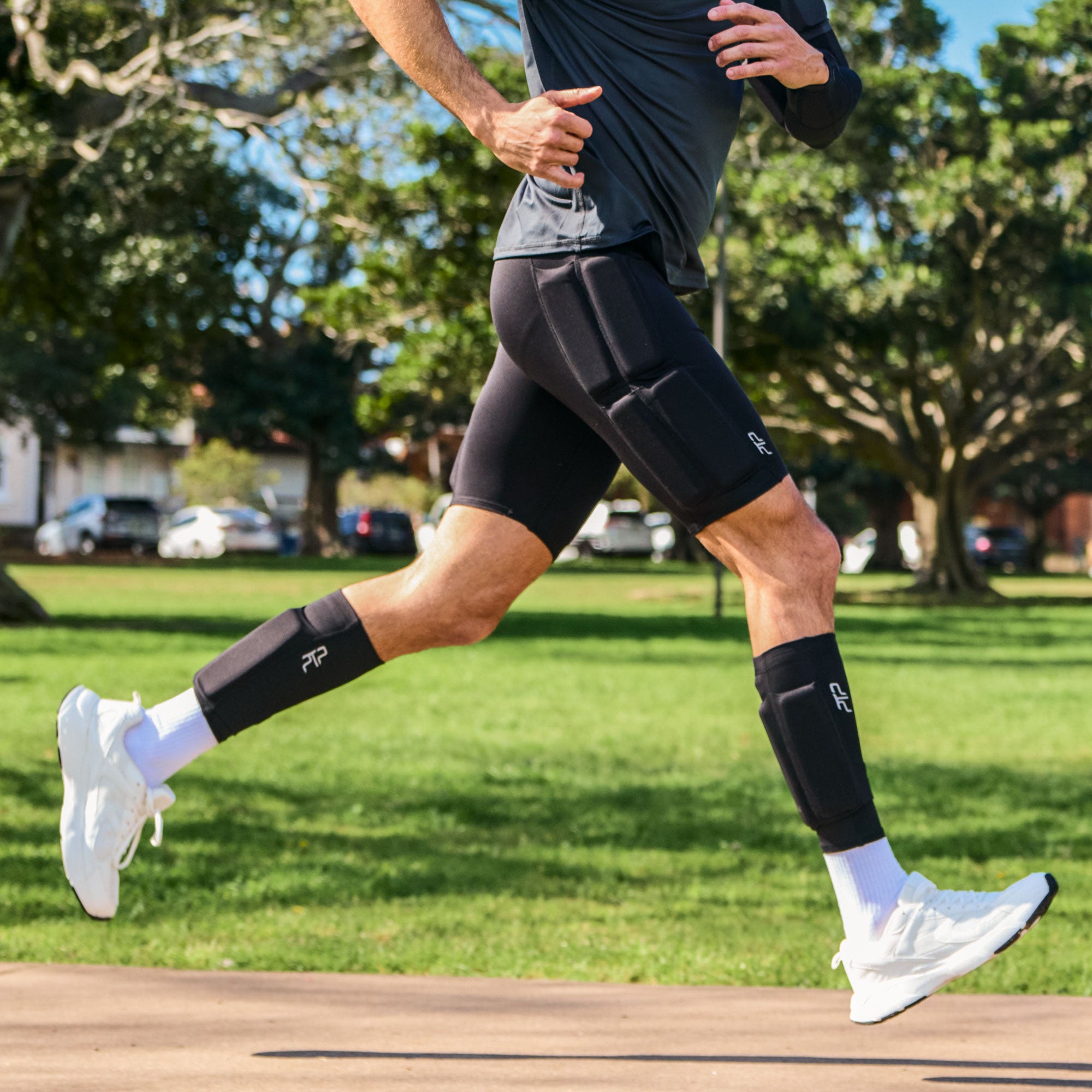 Man running on a park path while wearing black PTP Motion Microweighted Calf Sleeves.
