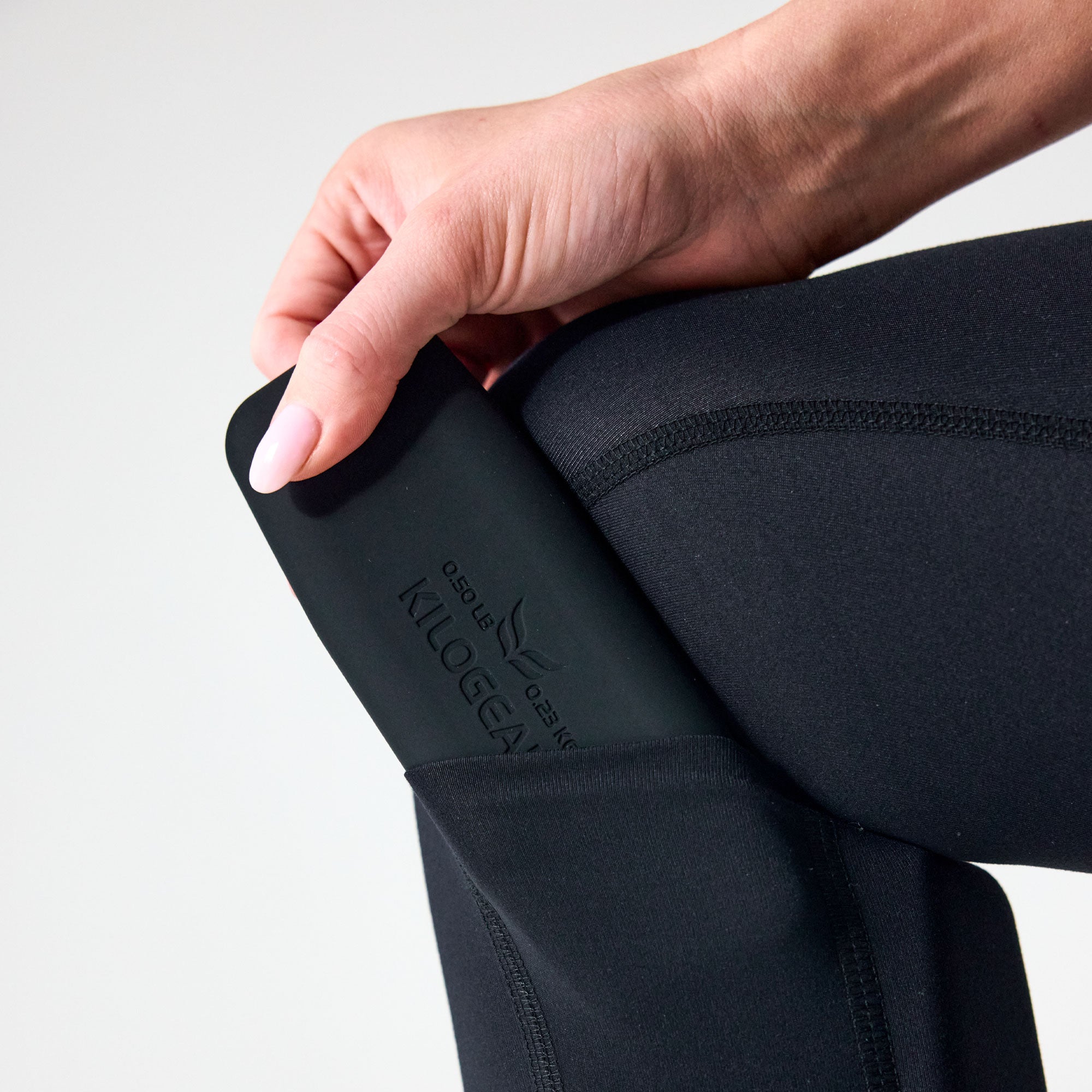Close-up of a PTP Large Pocket Weight being inserted into a calf pocket on black leggings.