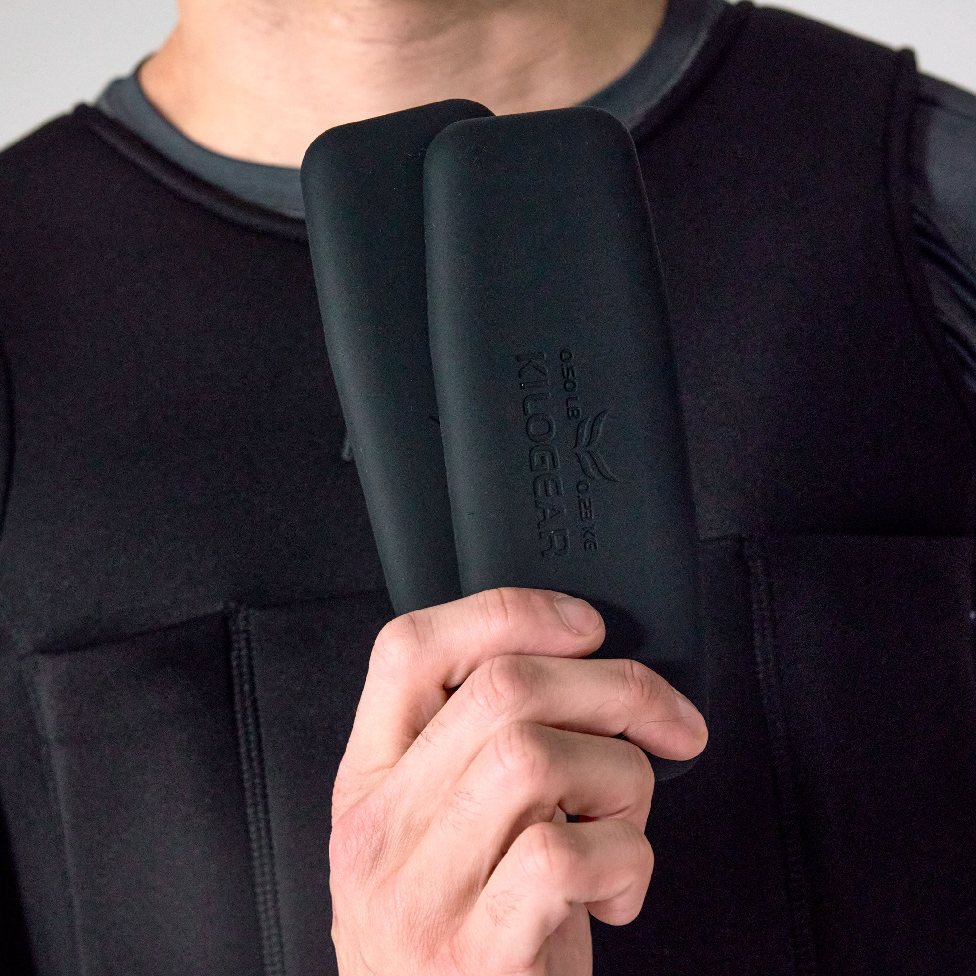 Man holding two black PTP Large Pocket Weights in front of a weighted vest.