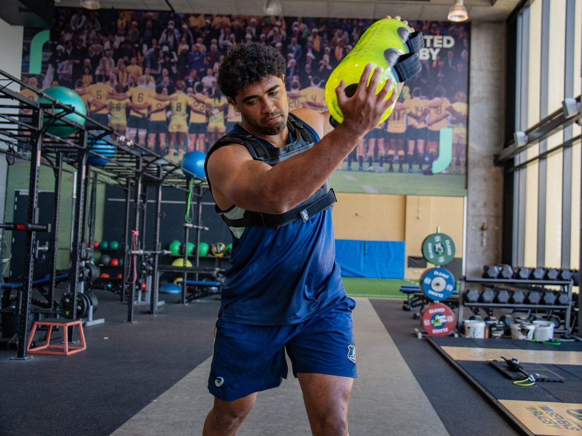 Rugby player pressing a lime PTP Aquacore overhead in a gym lined with Wallabies murals